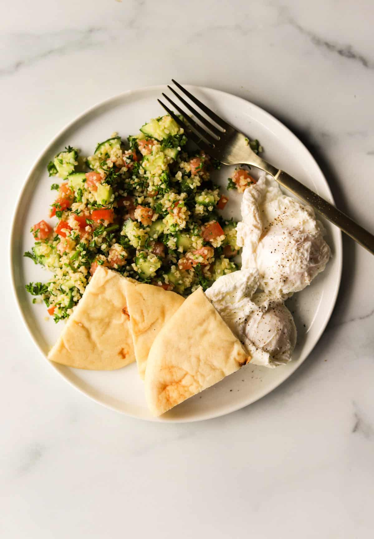 An overhead shot of a plate of tabouli with poached eggs and pita.