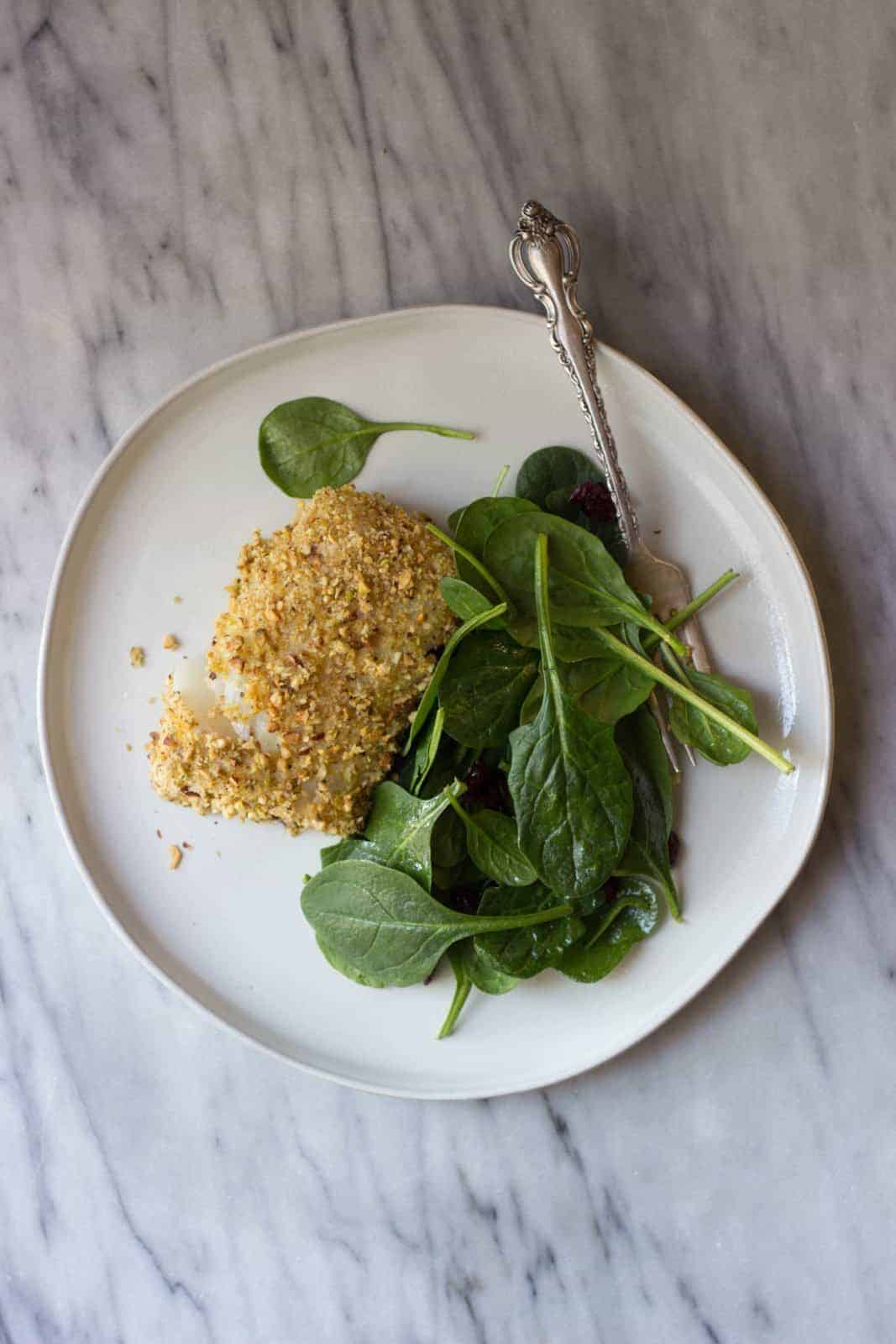 Pistachio-crusted cod sitting on a bed of spinach.