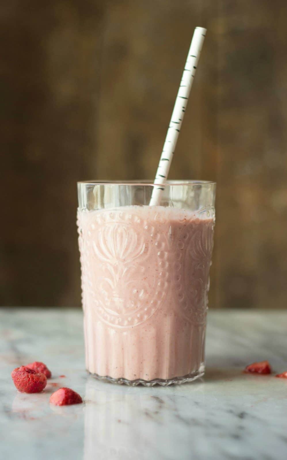 Side view of one strawberry banana cashew smoothie in a clear glass cup with a straw.