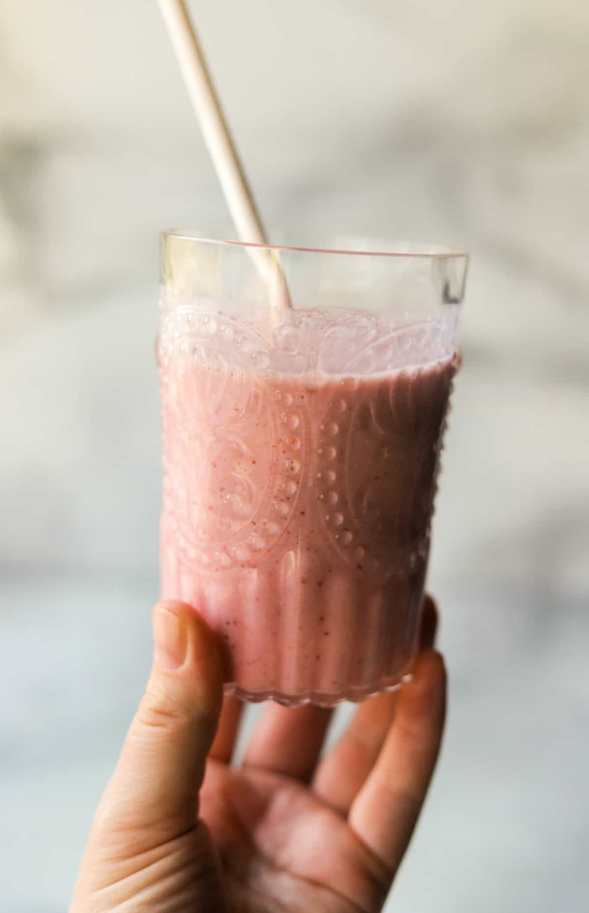 A front shot of a glass with a strawberry cashew smoothie with a white straw in it.