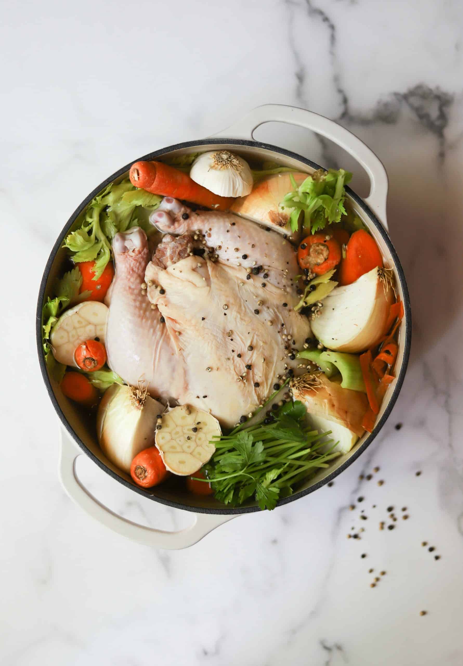 Chicken stock ingredients in a white Dutch oven