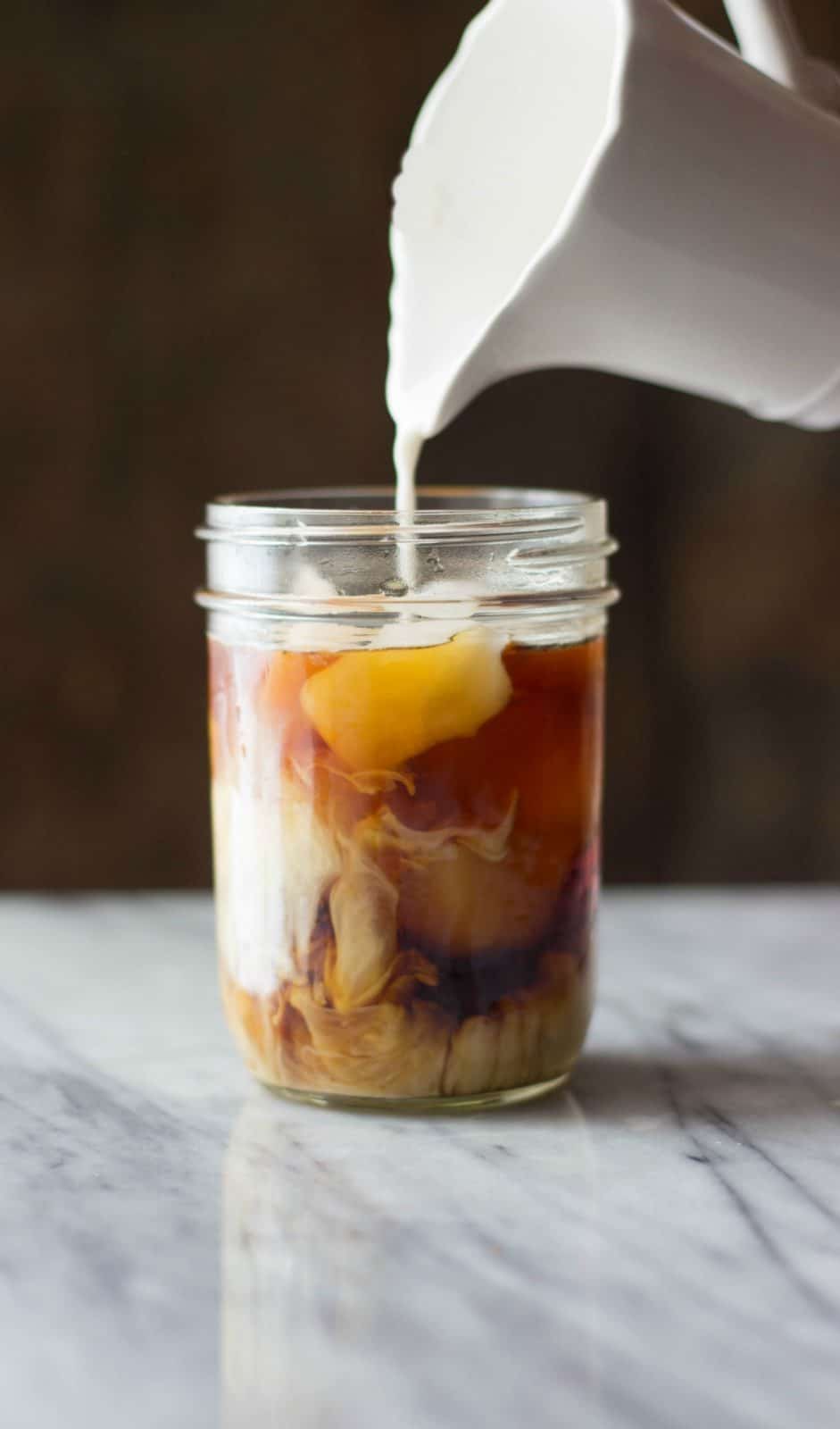 Coconut milk being pour into Cold Brew Coffee in a mason jar.