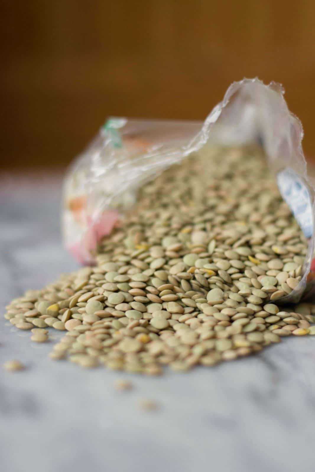 Close up of a bag of lentils opened with lentils spilling onto marble counter.
