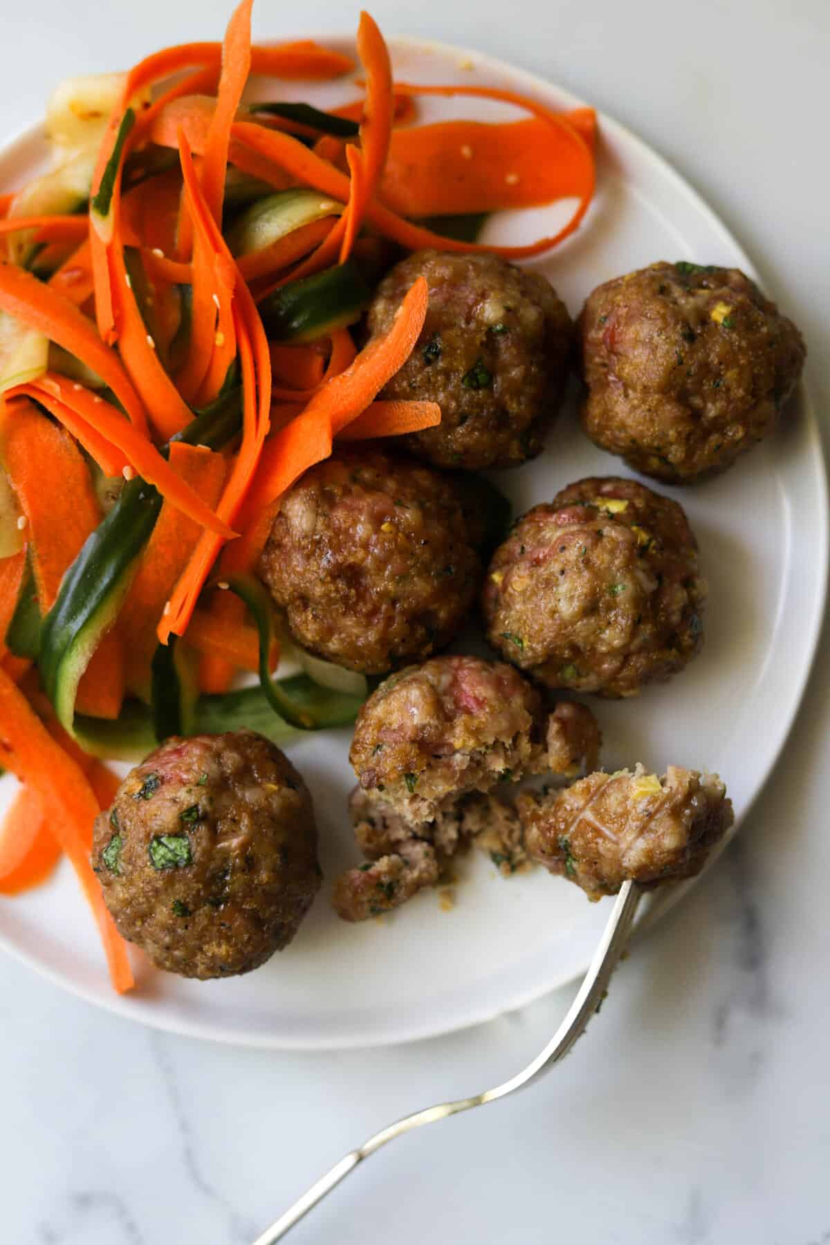 An overhead close up shot of a plate of sesame ginger meatballs with cucumber carrot salad.