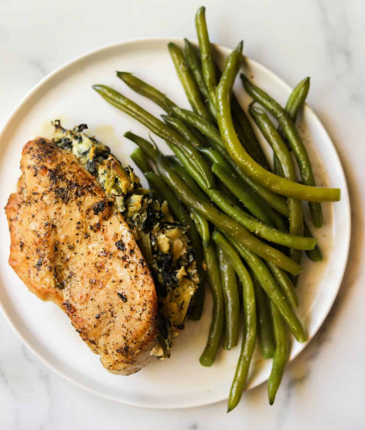 An overhead shot of a plate of spinach artichoke stuffed chicken breast and green beans.