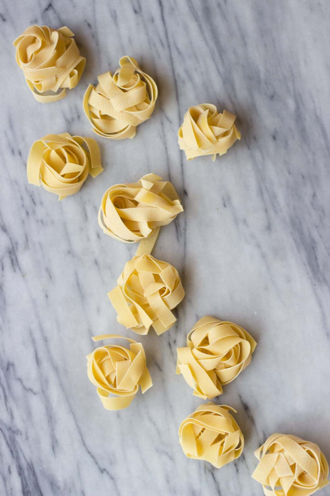 Uncooked Tagliatelle pasta on white marble. 
