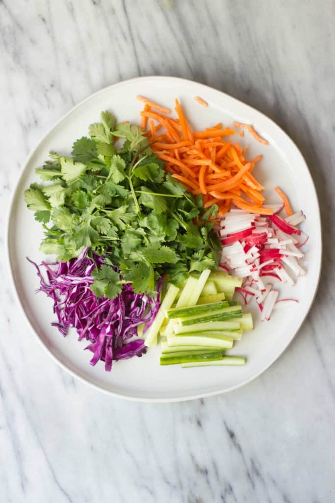 Overhead shot of crispy fresh vegetables prepared and ready to go into the rolls on a white plate. 