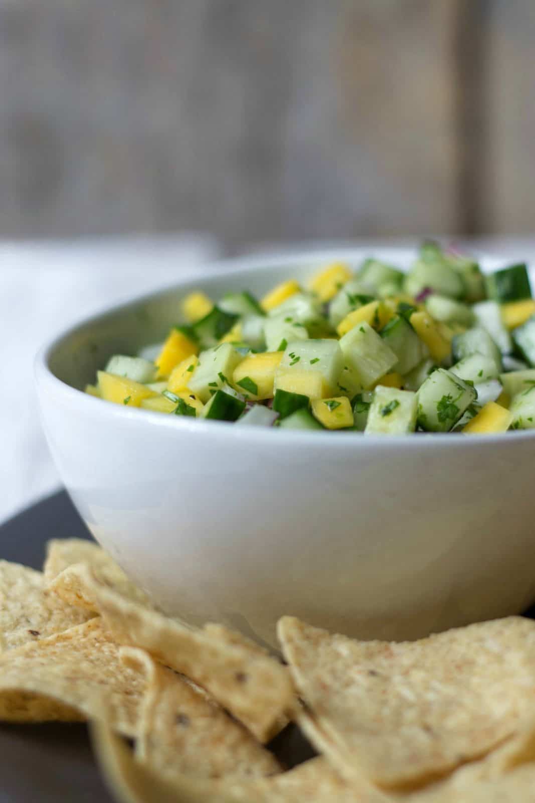 Side shot of Mango Cucumber Salsa in a white bowl next to tortilla chips.