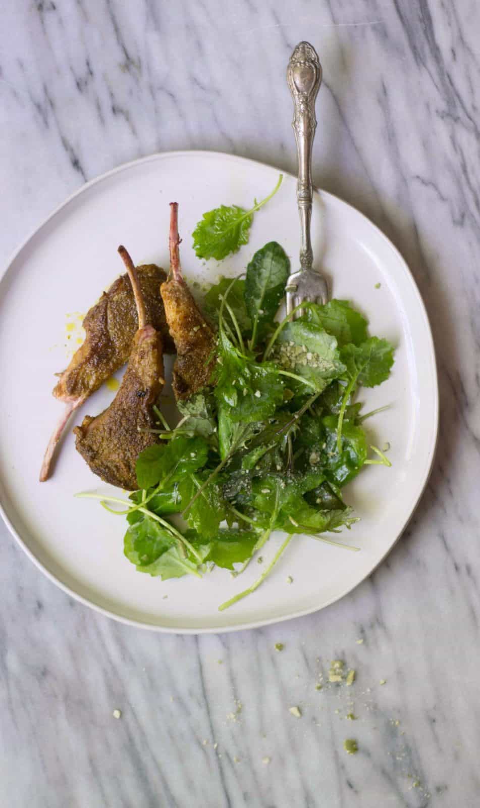 Finished Moroccan Lamb Lollipops with a side of greens on a white plate.