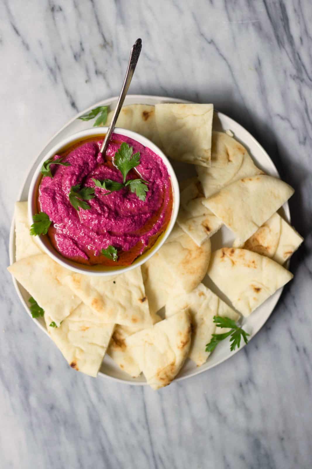 Beet Hummus in a white bowl with pita on a white plate.