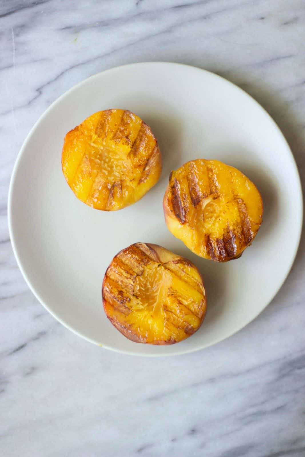 Grilled peaches on a white plate.