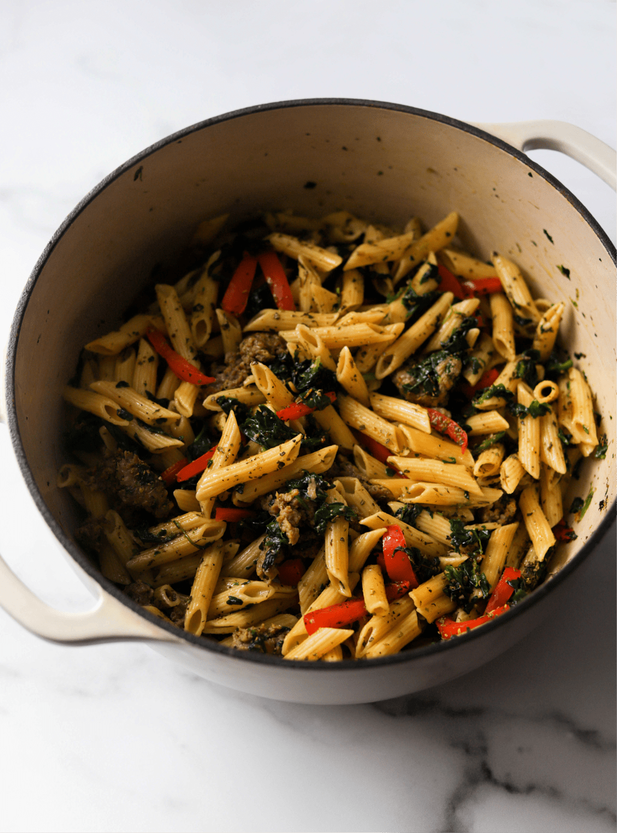 A side shot of a pot of pasta with sausage, spinach, bell peppers and Cajun and Italian seasonings.