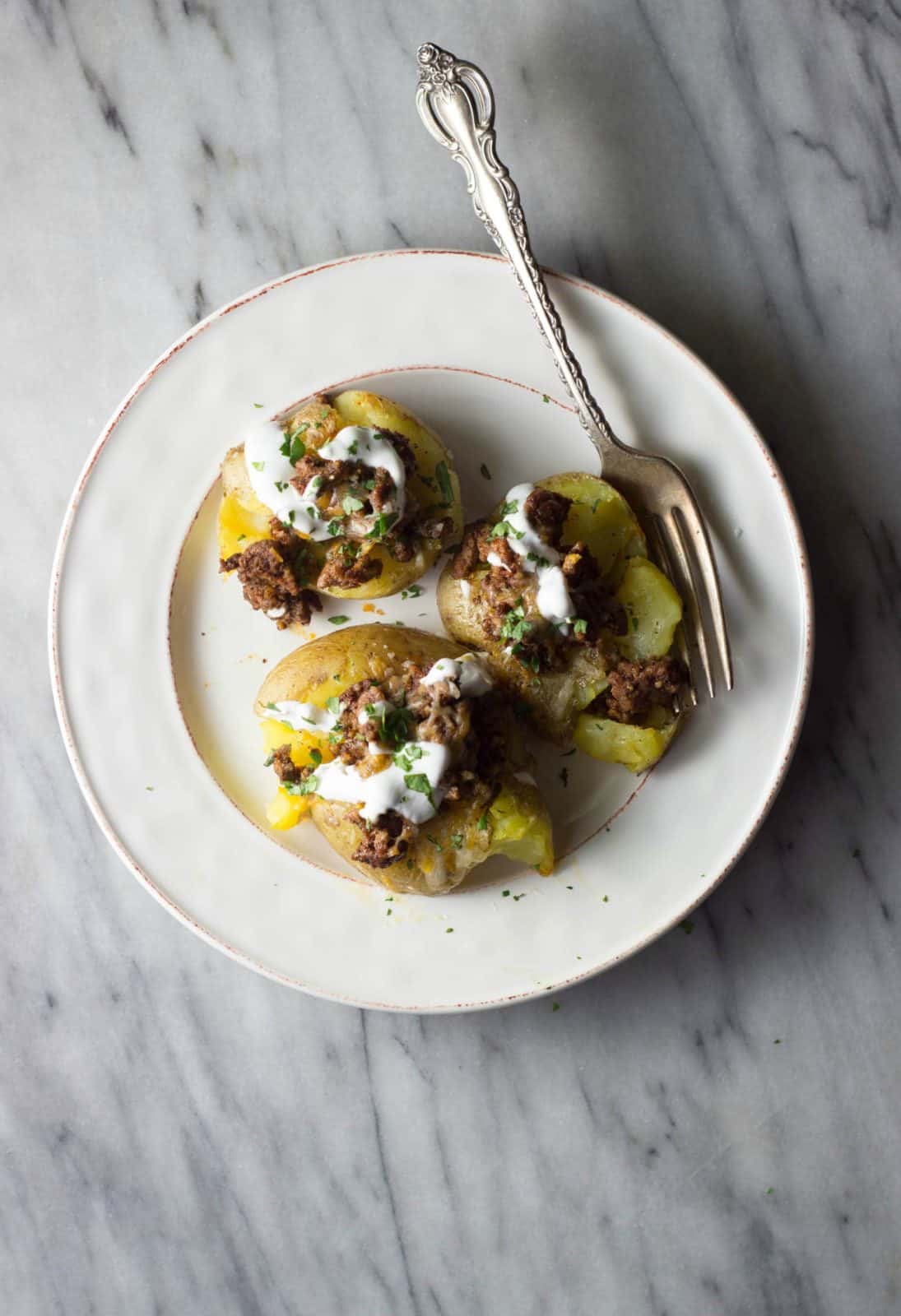 Taco-stuffed smashed potatoes on a white plate.