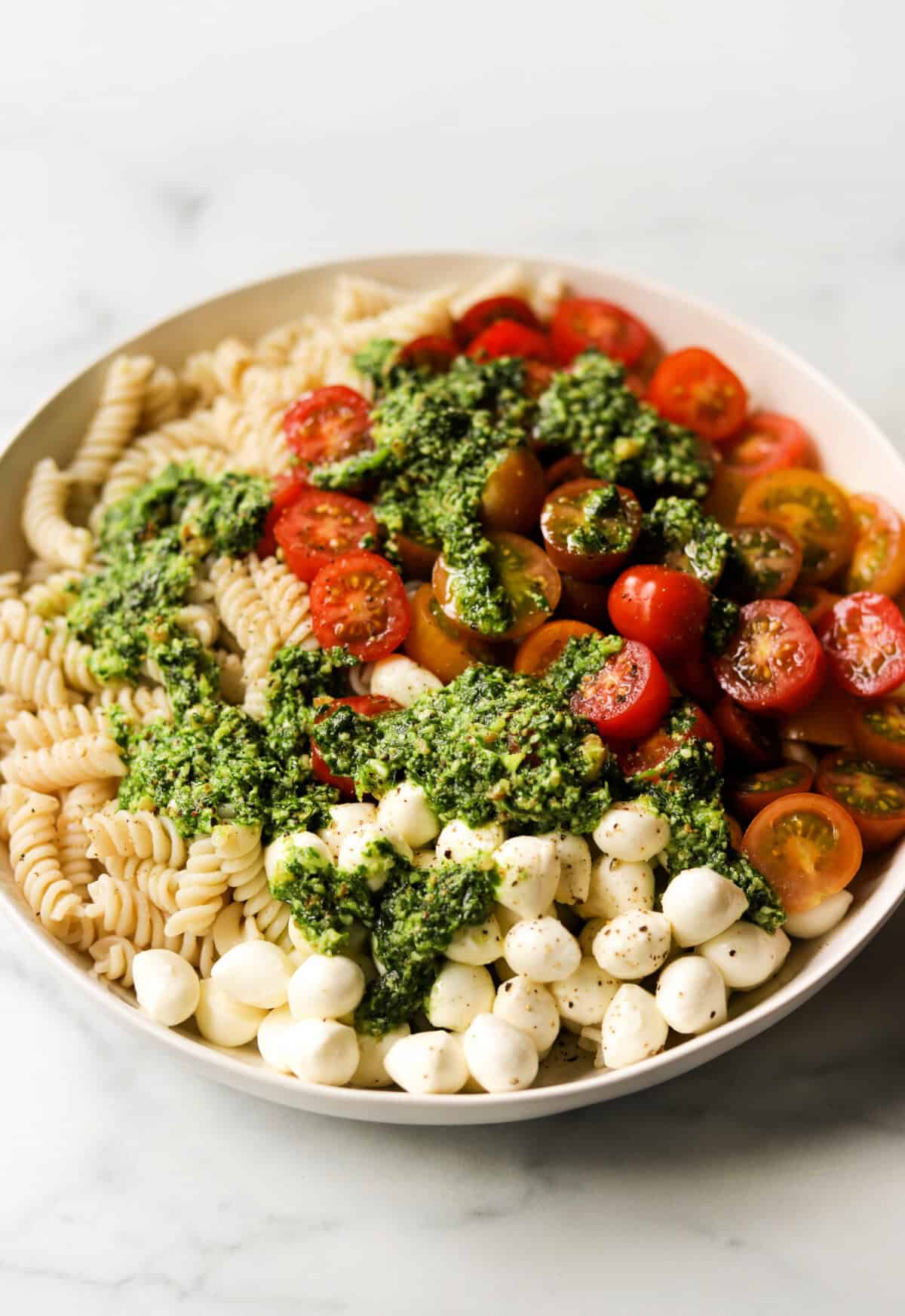 A front angled shot of a bowl of caprese pesto pasta salad.