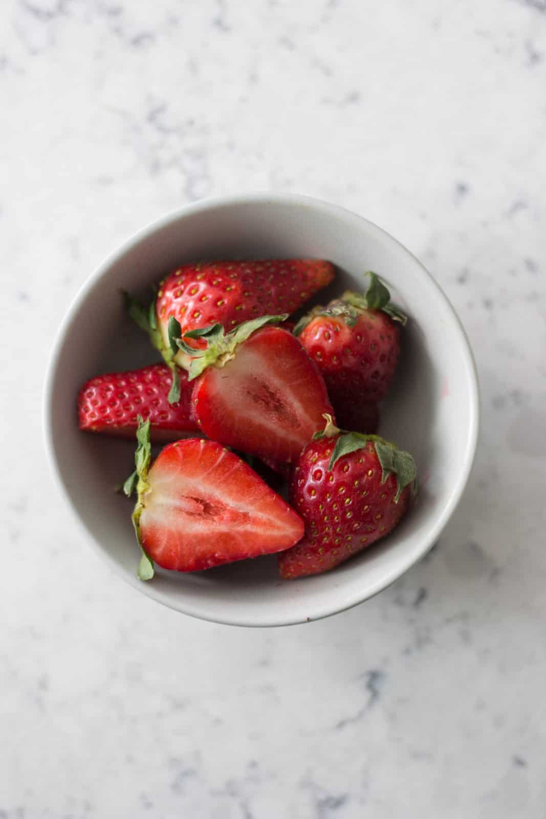 Fresh strawberries sliced in half in a white bowl
