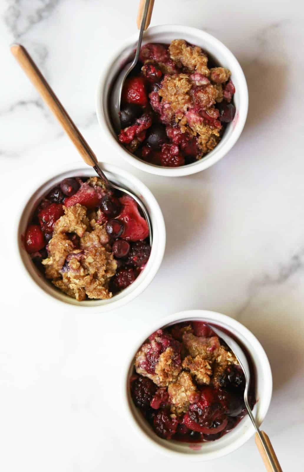 Mixed berry crisp in white dishes with spoons