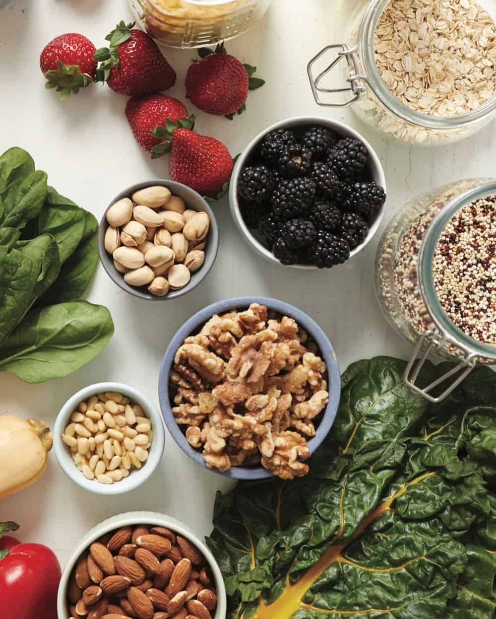 Overhead shot of bulk oats, quinoa, greens, nuts, and leafy greens. 