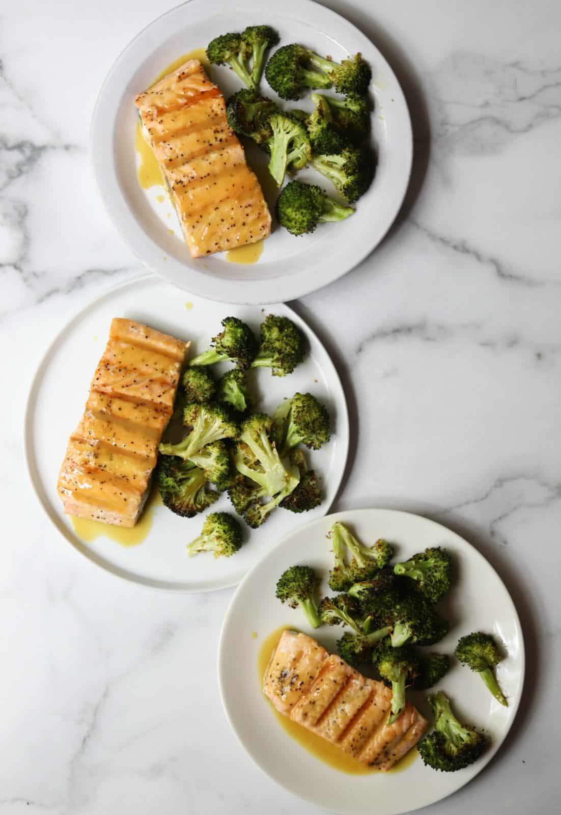 An overhead shot of white plates with maple mustard salmon and roasted broccoli.