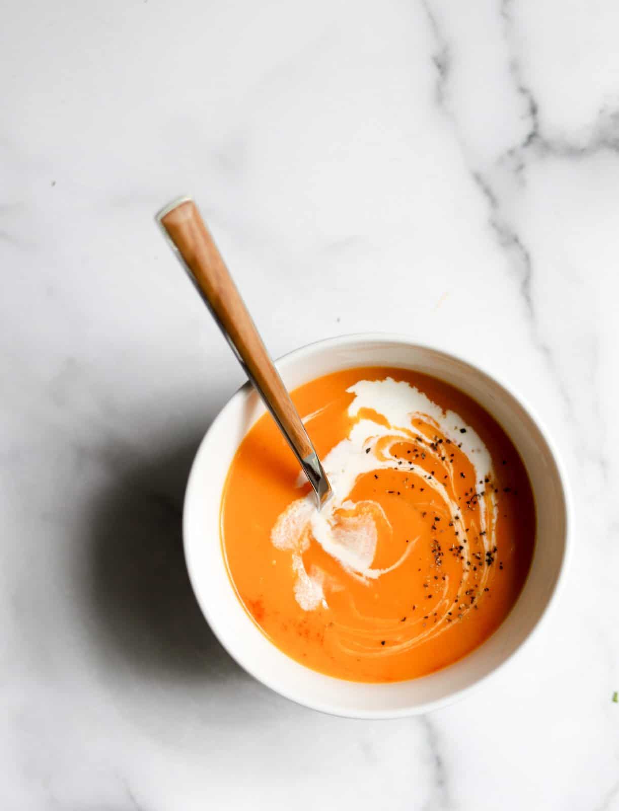 An overhead shot of a single bowl of curry sweet potato soup with coconut milk swirled in.