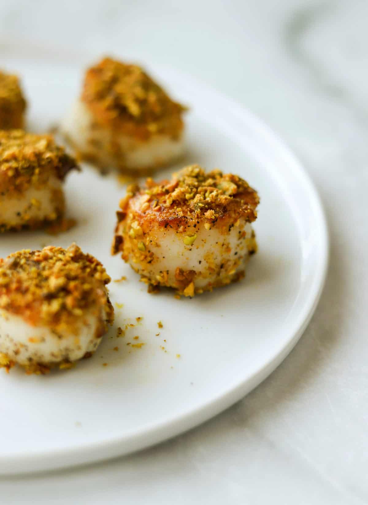 A side shot of a plate of pistachio crusted scallops.