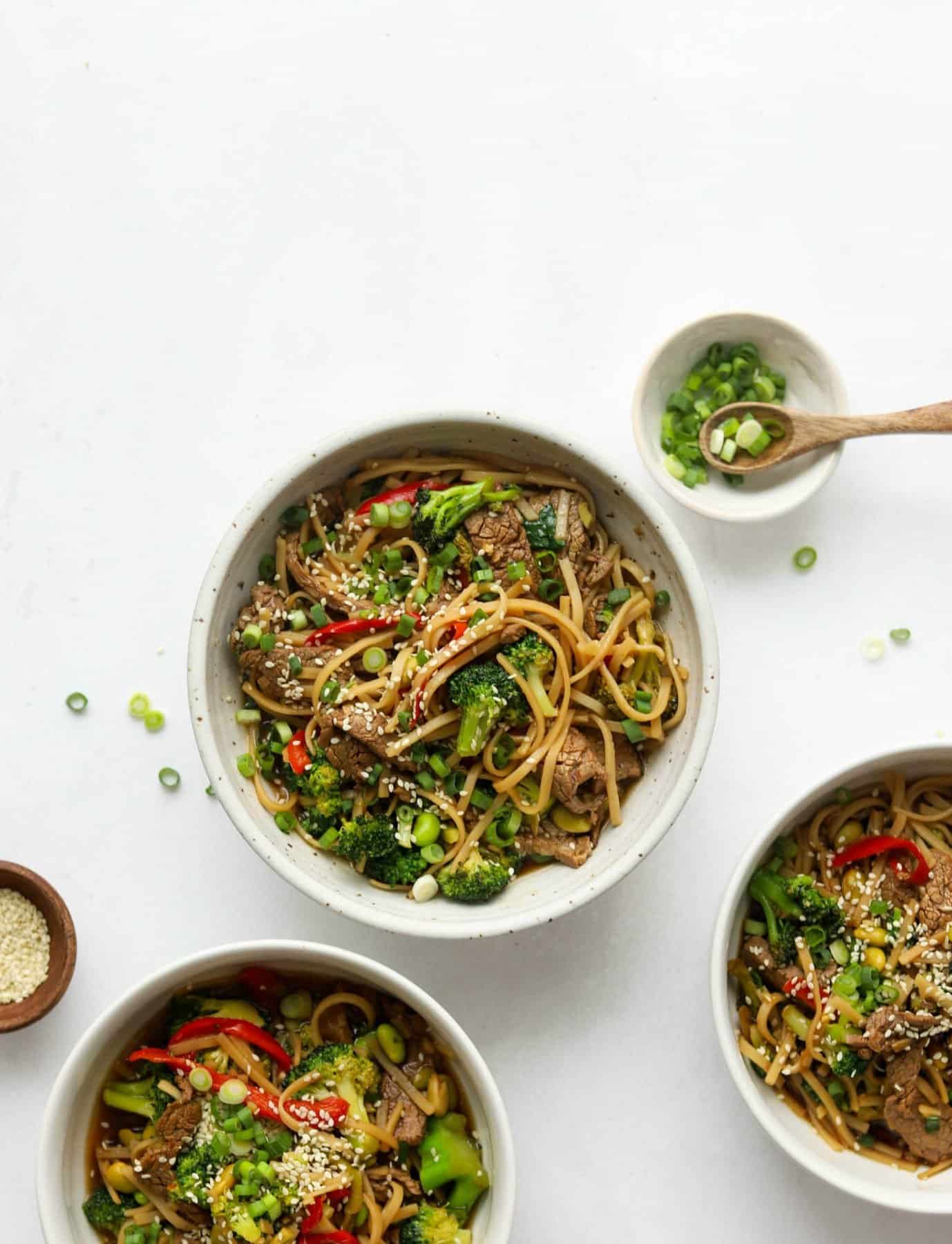 Overhead shot of Asian-Style Beef & Veggie Noodle Bowls in white bowls and chopped green onion on the side.