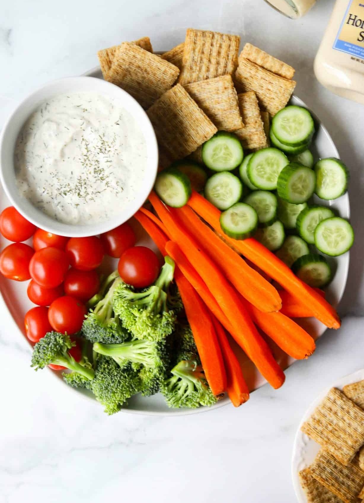 An overhead shot of a platter of crudites with a bowl of dill veggie dip.
