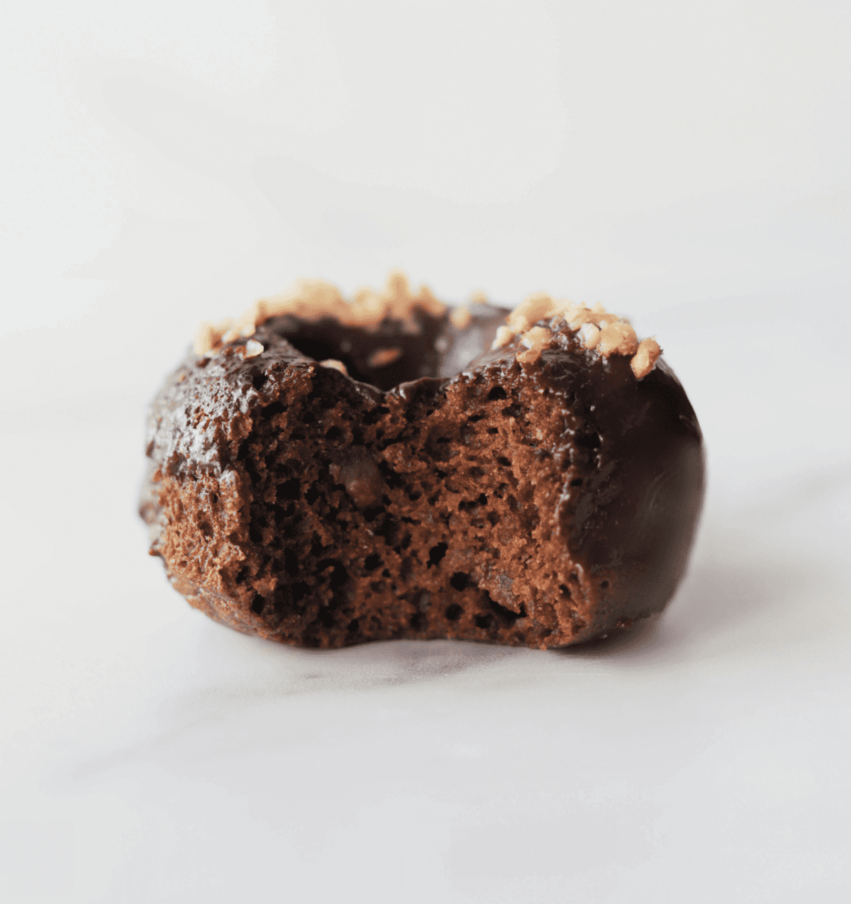 A front close up shot of a chocolate glazed donut with a bite taken out of it.