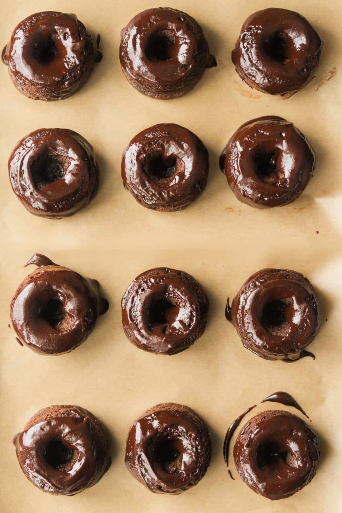 An overhead shot of chocolate glazed donuts lined on parchment paper.