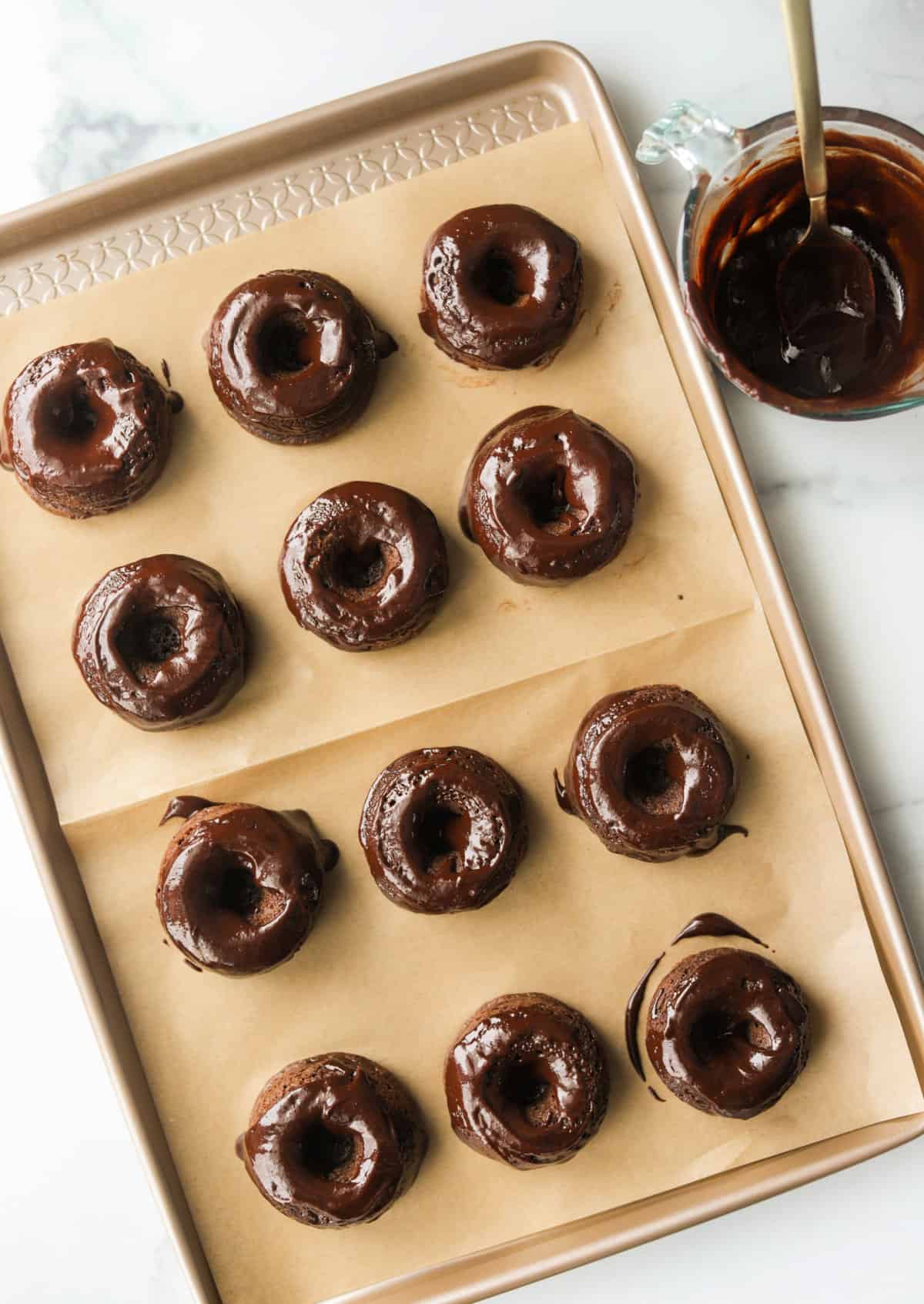 An overhead shot of chocolate avocado donuts on a sheet pan slathered with chocolate glaze.