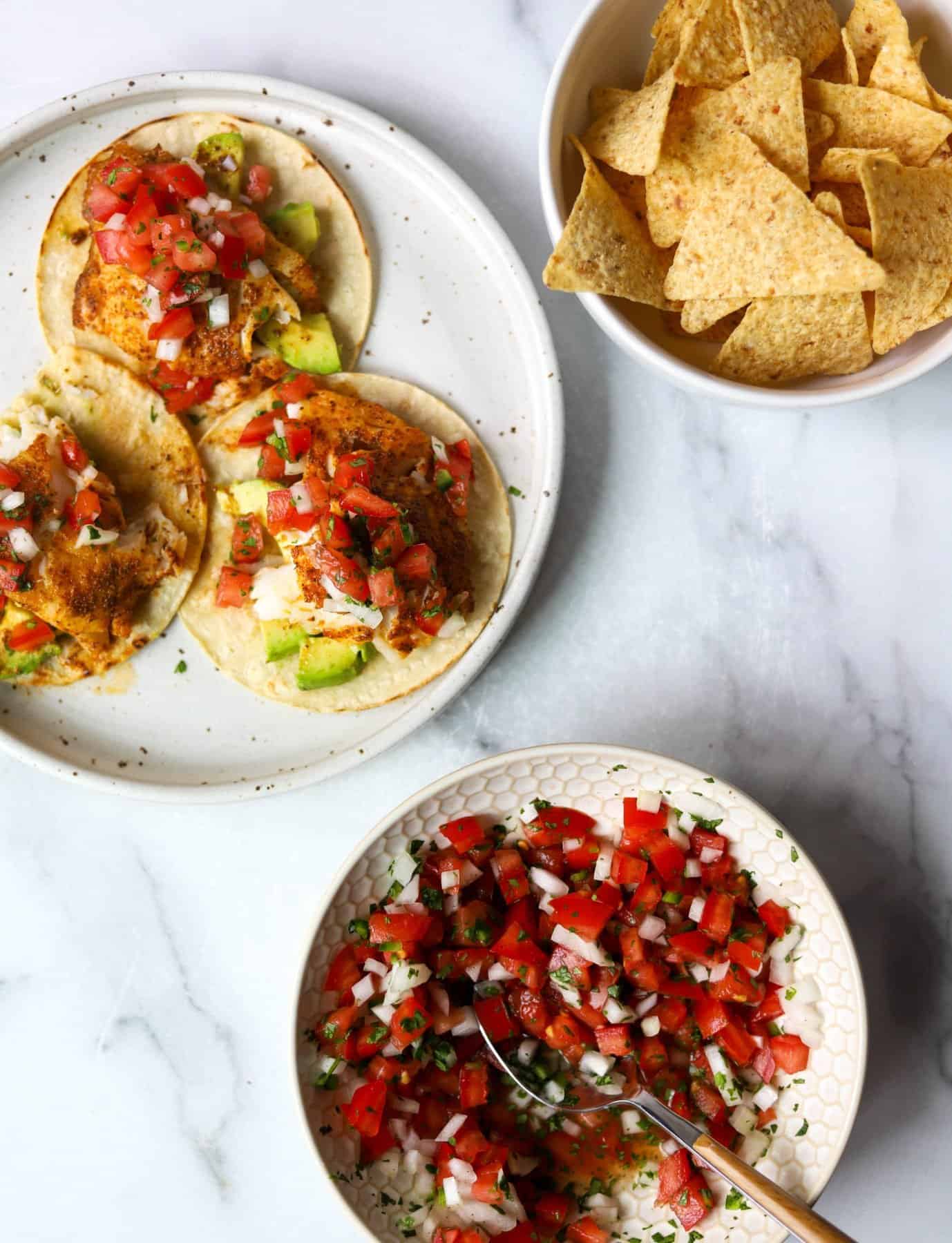 Blackened fish tacos with pico de gallo on a plate with tortilla chips and a bowl of pico