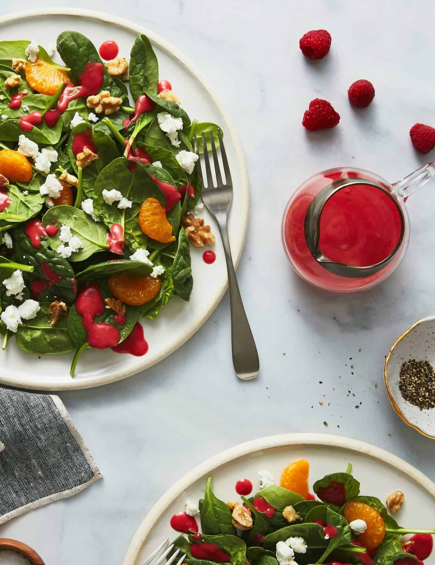 Salad on white plates with raspberry dressing in a carafe