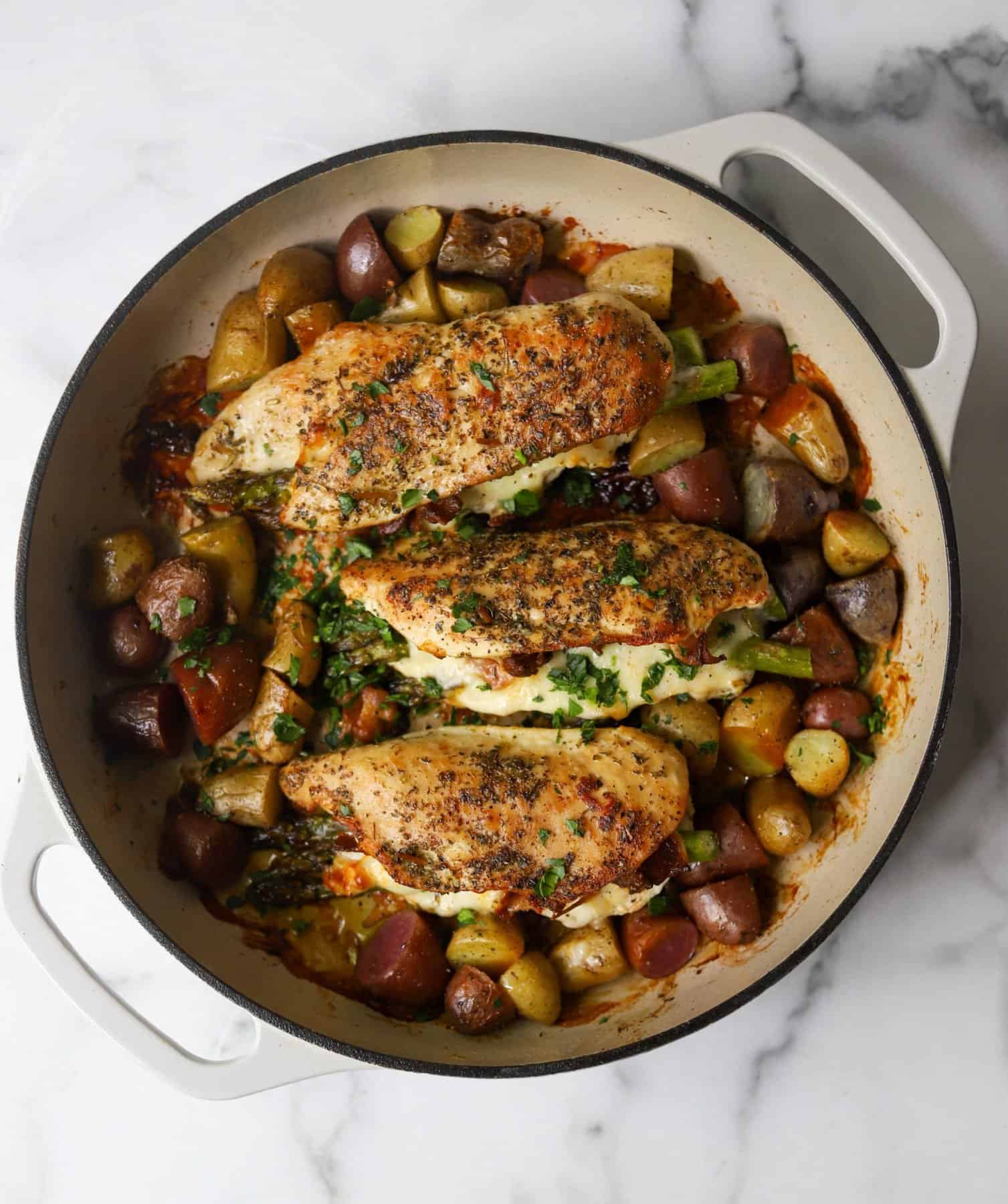 Asparagus stuffed chicken and potatoes in a white dish