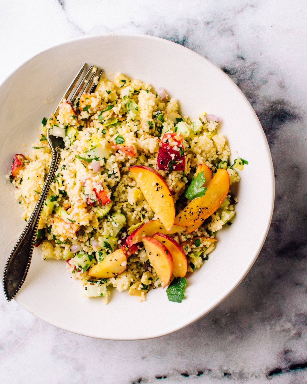 An overhead shot of a couscous salad with peaches and fresh herbs on top.