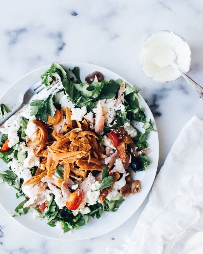 An overhead shot of a platter of fattoush salad with a bowl of creamy salad dressing on the side.