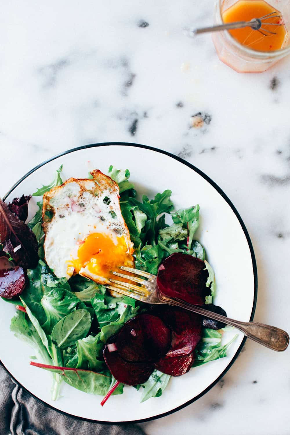 An overhead shot of a green breakfast salad with a fried egg on top.