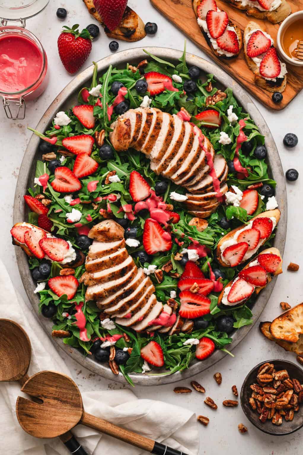 A large platter with an arugula salad with chicken slices, berries, ricotta roast and raspberry dressing drizzled on top.
