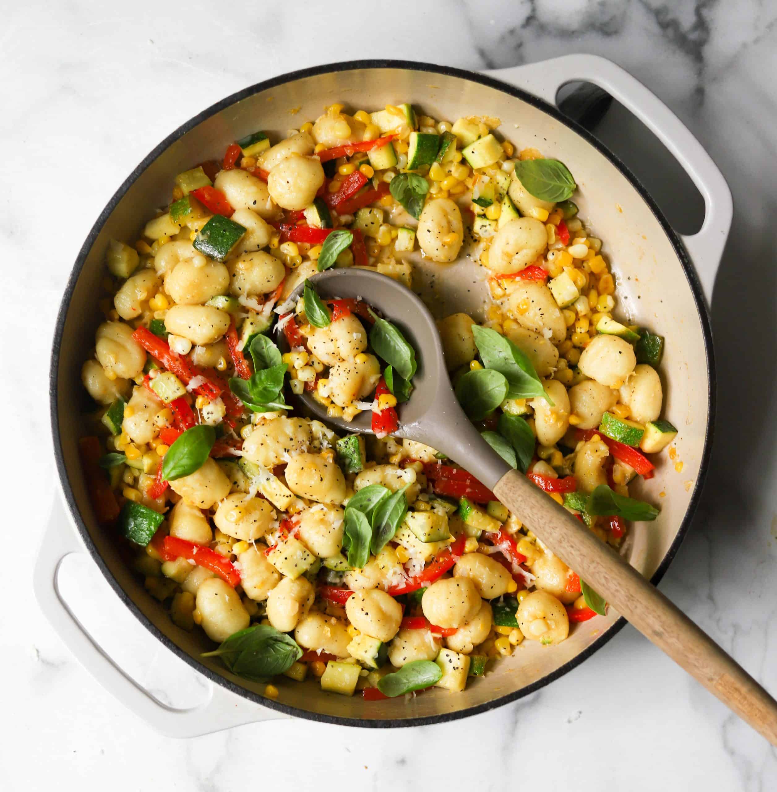 A white skillet filled with gnocchi zucchini and sweet corn with basil.