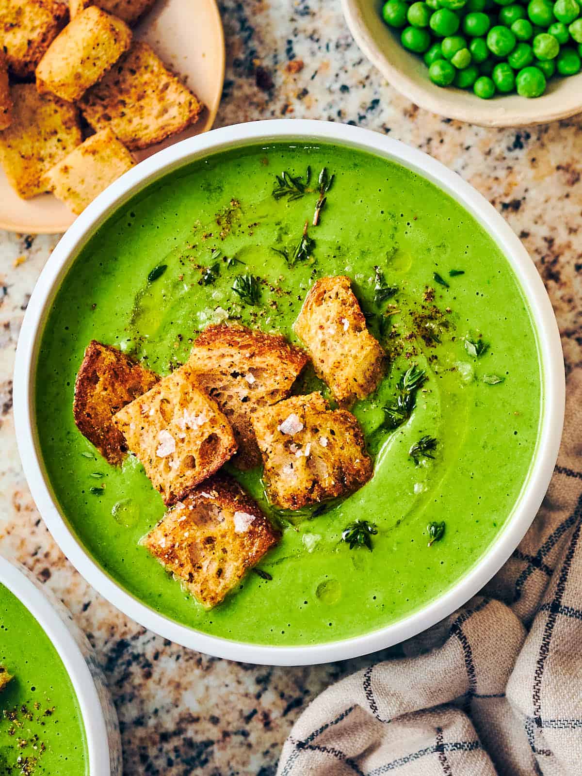 An overhead shot of a bowl of frozen pea soup with croutons.