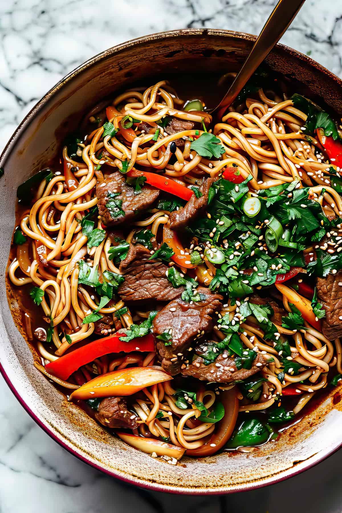 An overhead shot of a bowl of beef, noodles and vegetables with fresh herbs.