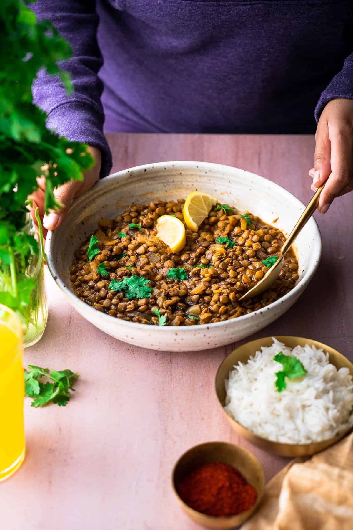 A front angled shot of a person spooning from a bowl of brown lentils.