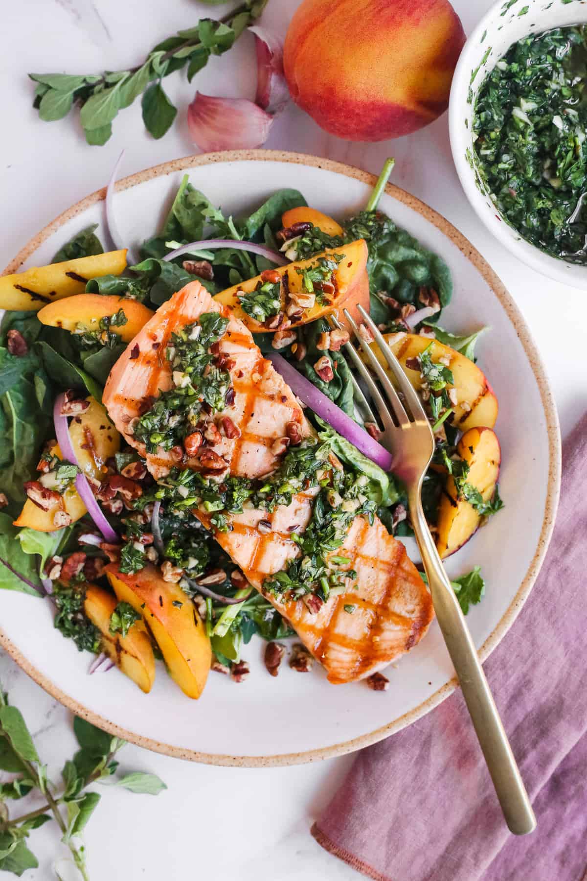 An overhead shot of a bowl of a green salad with salmon, peaches and chimichurri.