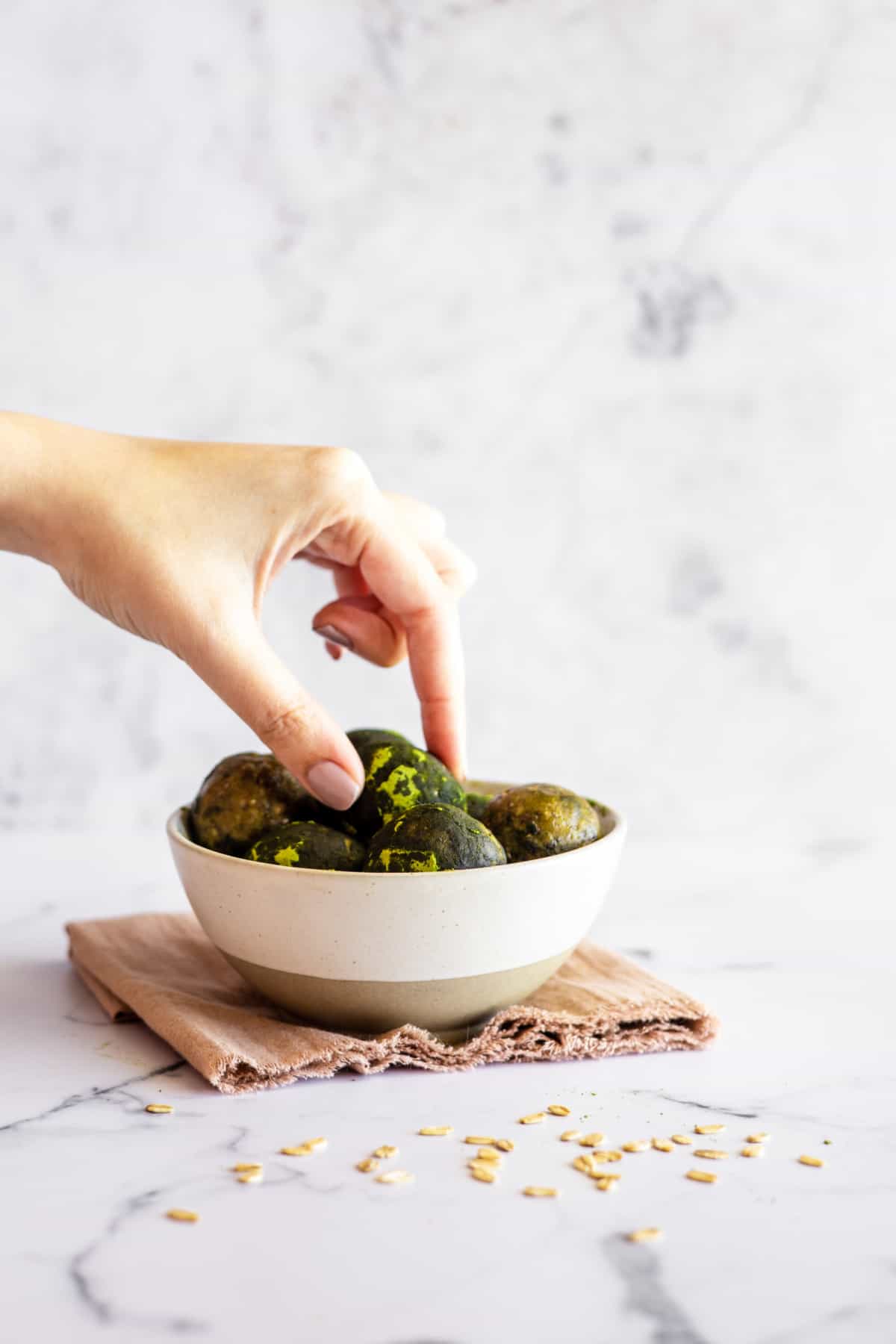 A front shot of a bowl of matcha energy balls with a hand reaching to grab one.