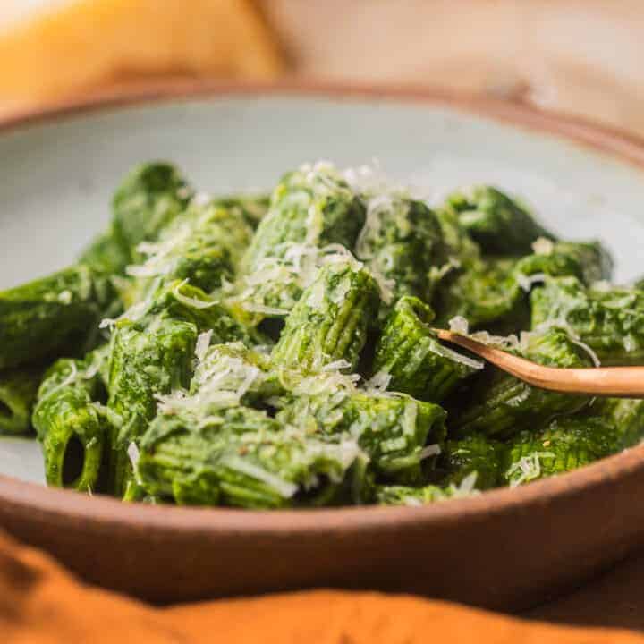 A front shot of a bowl of kale pesto pasta with a wooden spoon.