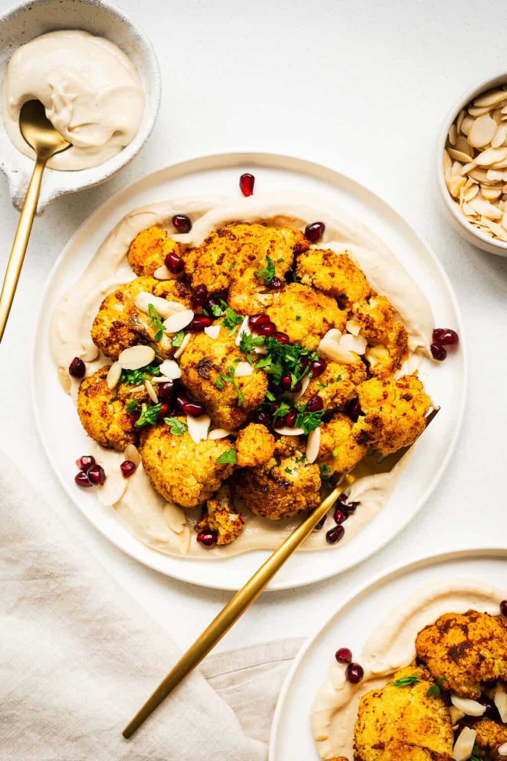 An overhead shot of a plate of roasted cauliflower with tahini sauce and pomegranates.