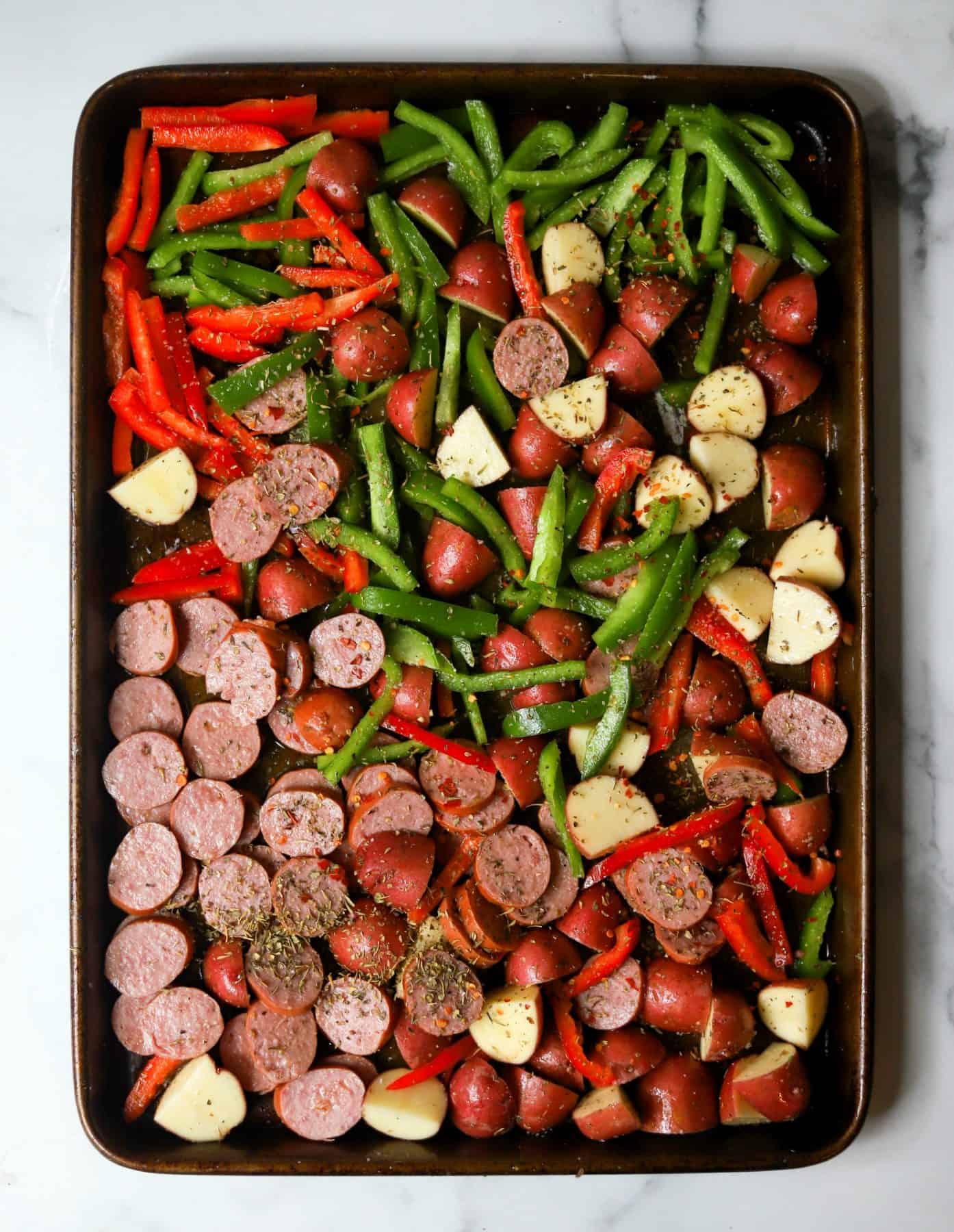 Sliced sausage, potatoes and bell peppers on a sheet tray.