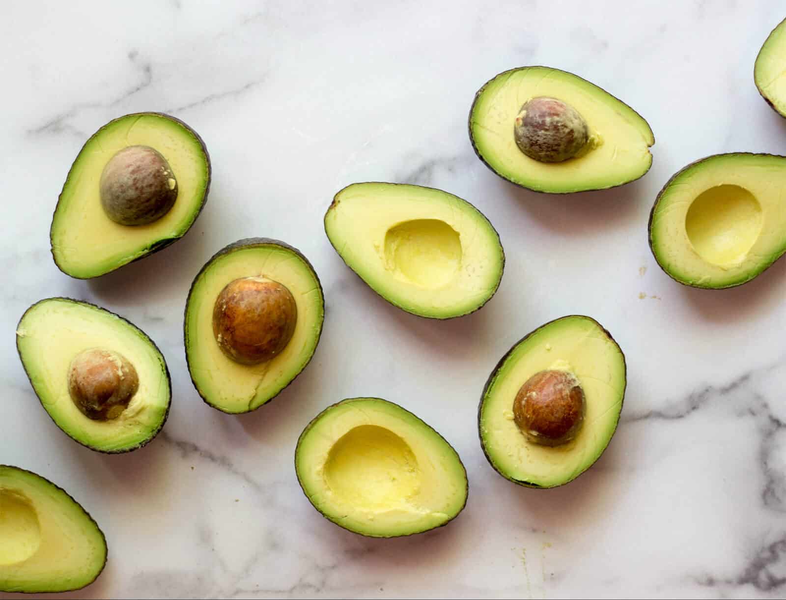 Halved avocados on a white marble board.