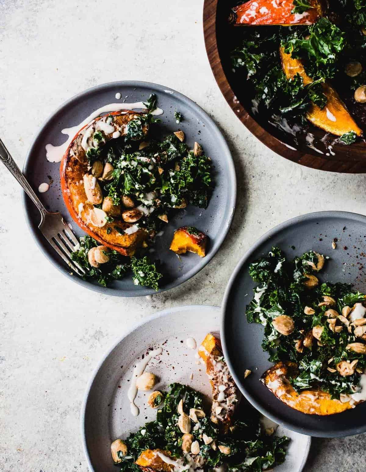 An overhead shot of bowls of red kuri squash with kale and nuts.