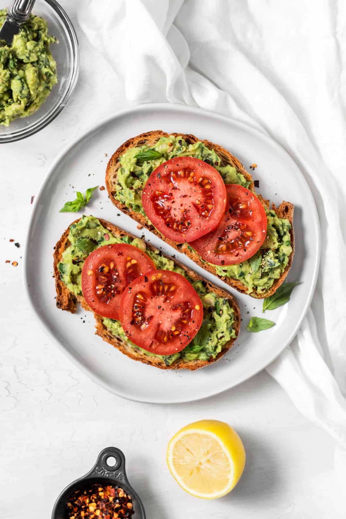 An overhead shot of avocado toast with slices of tomato on top.