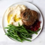 Beef tenderloin, green beans, mashed potatoes and cranberry compote on a white plate