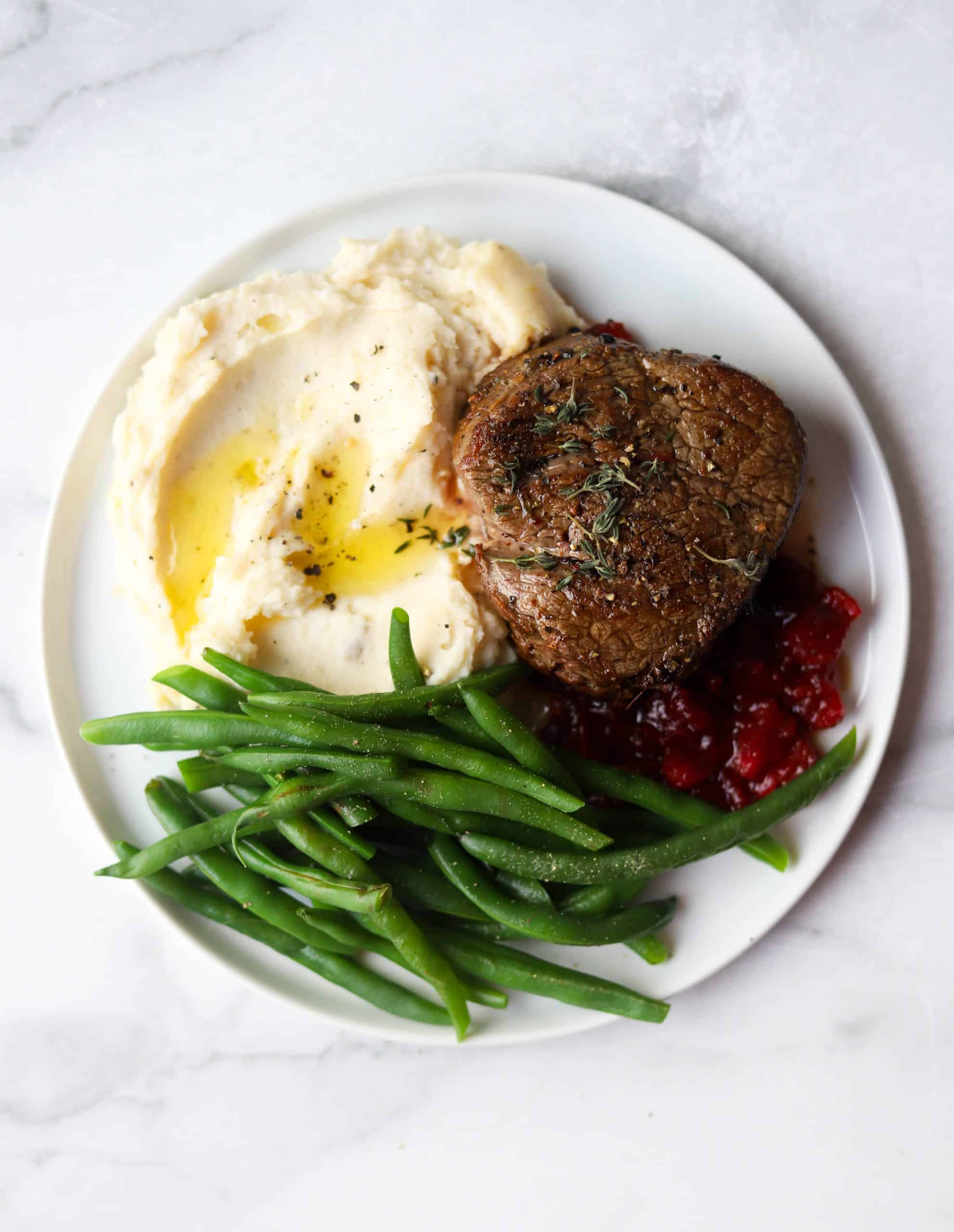 Beef tenderloin, green beans, mashed potatoes and cranberry compote on a white plate